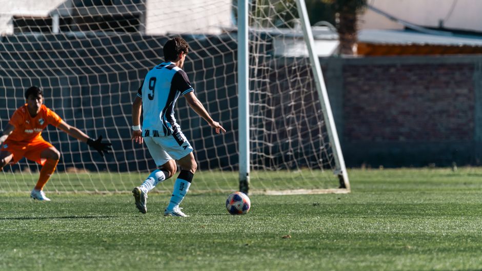 Soccer player in action taking a shot towards goal with goalkeeper ready to defend.